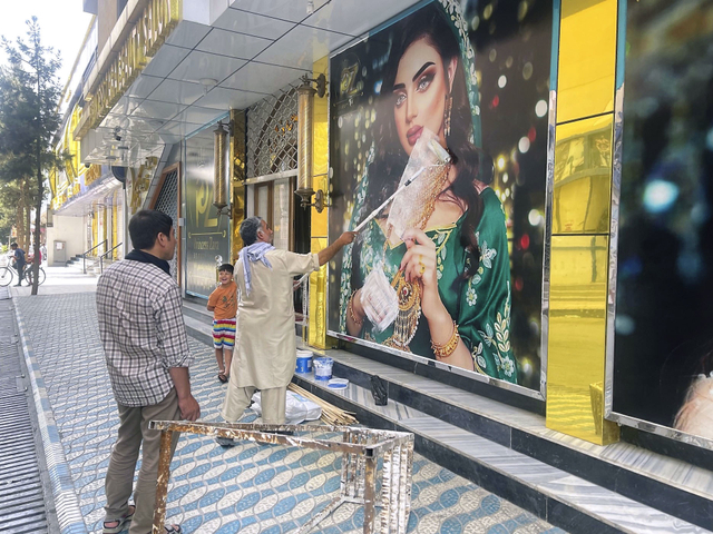 Seorang pekerja menghapus foto reklame seorang wanita di dinding salon kecantikan di Kabul. Foto: Reuters