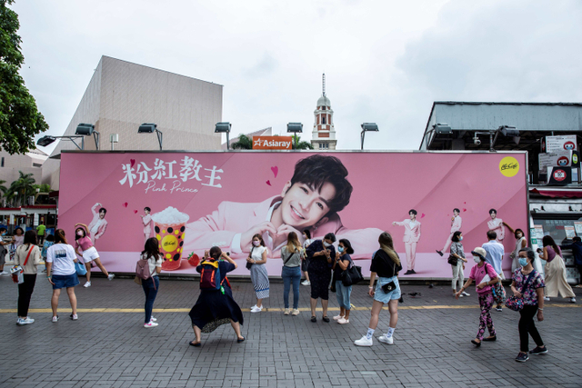 Fans Miror berfoto di depan papan iklan yang menunjukkan potret Anson Lo, anggota boyband Cantopop Mirror, di Hong Kong. Foto: Isaac Lawrence/AFP