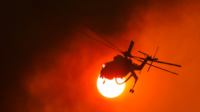 Helikopter pemadam kebakaran terbang di dekat matahari saat api membakar di desa Vilia, Yunani, Rabu (18/8). Foto: Alkis Konstantinidis/REUTERS