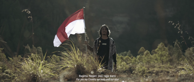 Alffy Rev mebawa bendera merah putih di atas bukit. Foto: Tangkapan Layar dalam "Wonderland Indonesia".