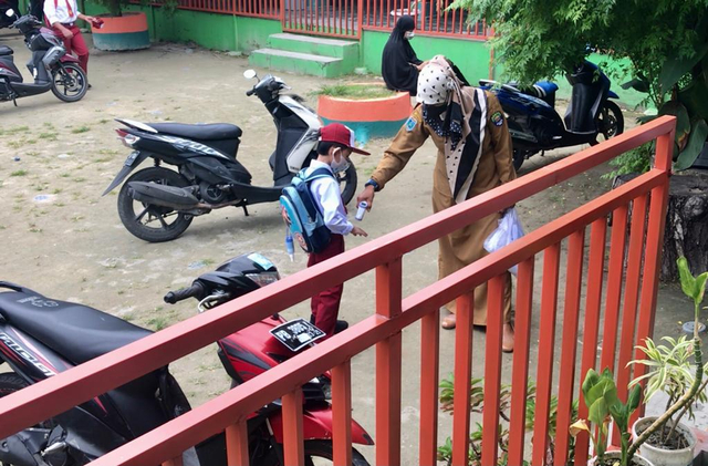 Guru Pada SD Yapis Kaimana, Tengah Mengukur Suhu Tubuh Salah Seorang Siswa Sebelum Masuk ke Dalam Ruang Kelas