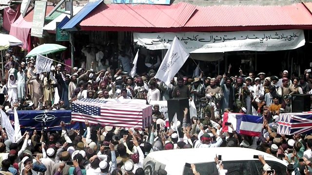 Kerumunan membawa peti mati yang dibungkus dengan bendera NATO, AS, dan Union Jack selama pemakaman pura-pura di sebuah jalan di Khost, Afghanistan, Selasa (31/8). Foto: ZHMAN TV/via REUTERS