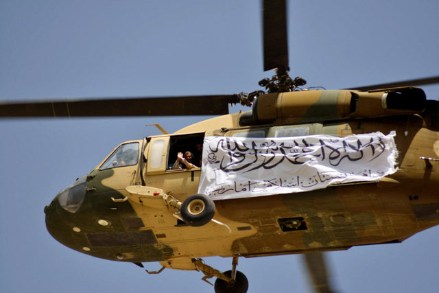 Sebuah helikopter mengibarkan bendera Taliban terbang di atas pendukung yang merayakan penarikan pasukan Amerika Serikat dari Afghanistan di Kandahar, Afghanistan. Foto: JAVED TANVEER / AFP
