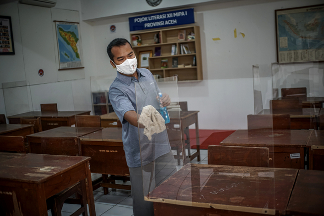 Penjaga sekolah membersihkan ruang kelas SMAN 81 Jakarta Timur jelang penambahan sekolah yang menggelar pembelajaran tatap muka (PTM) pada Senin, (13/9). Foto: Iqbal Firdaus/kumparan