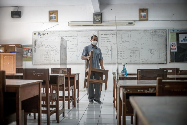 Penjaga sekolah merapikan ruang kelas SMAN 81 Jakarta Timur jelang penambahan sekolah yang menggelar pembelajar tatap muka (PTM) pada Senin, (13/9). Foto: Iqbal Firdaus/kumparan