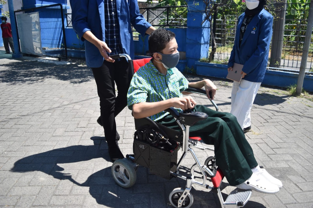 Salah satu siswa SLB YPAC Surabaya saat mencoba menggunakan Kursi Roda Elektrik dibantu oleh tim KKN Abmas ITS.