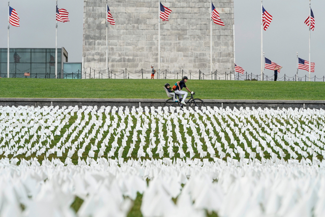 Warga mengendarai sepeda melewati bendera putih yang mewakili orang Amerika yang telah meninggal karena virus corona yang ditempatkan di National Mall, Washington, Amerika Serikat.  Foto: Joshua Roberts/REUTERS