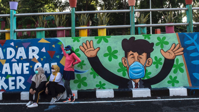 Warga berfoto dengan latar belakang mural yang mengajak warga untuk memakai masker di tengah pandemi COVID-19 di Surabaya. Foto: Juni Kriswanto/AFP