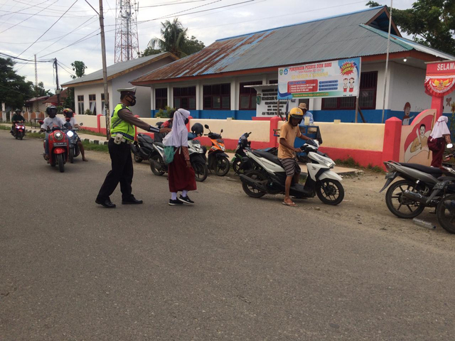 Polantas di Kepulauan Sula saat membantu seorang siswa menyeberangi jalan utama. Foto: Iwan Setiawan/cermat