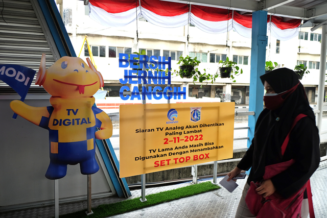 Calon penumpang TransJakarta melintas di depan Iklan Layanan Masyarakat untuk program Migrasi TV Digital di Halte Harmoni, Jakarta Pusat, Jumat, 20 Agustus 2021. Foto: Kominfo