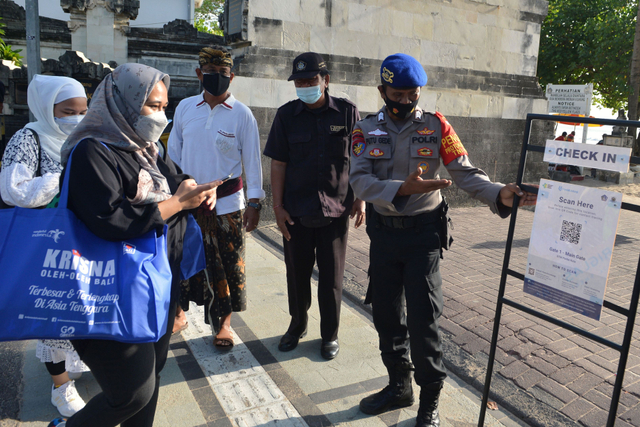 Petugas mengarahkan wisatawan untuk memindai QR Code dengan aplikasi PeduliLindungi sebelum memasuki kawasan wisata Pantai Kuta, Badung, Bali, Minggu (26/9/2021). Foto: Fikri Yusuf/Antara Foto