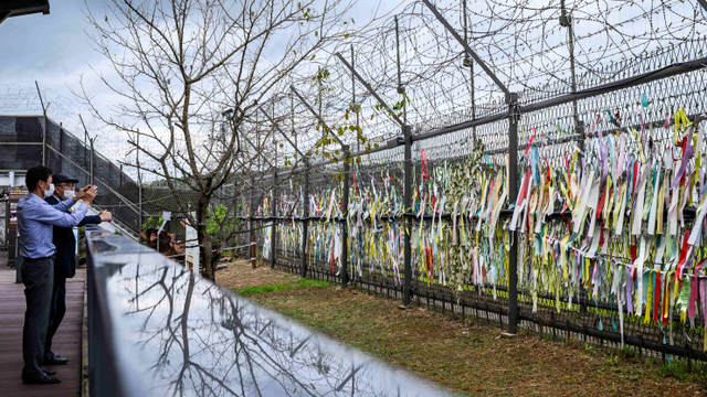 Pengunjung mengambil foto pagar yang dihiasi pita dengan pesan tertulis di atasnya, di 'taman perdamaian' Imjingak dekat Zona Demiliterisasi (DMZ) yang memisahkan Korea Utara dan Selatan. Foto: Anthony Wallace/AFP