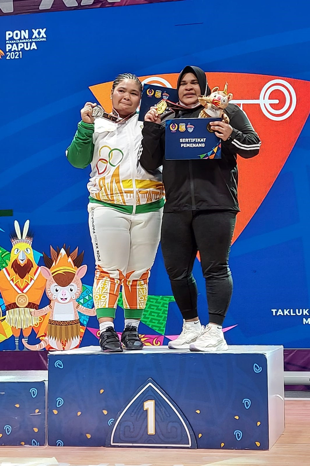 Lifter Aceh Nurul Akmal (berhijab) berbagi podium kemenangan dengan lifter Kalimantan Barat Riska Oktaviana usai tampil di kelas +87 kg cabor angkat besi putri PON XX Papua 2021. Foto: Dok. Humas KONI Aceh