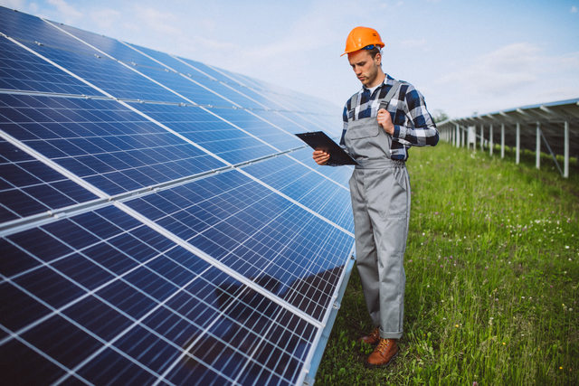 Teknisi PLTS sedang memeriksa performa PLTS (https://www.freepik.com/free-photo/man-worker-firld-by-solar-panels_5176442.htm#page=1&query=solar&from_query=solar%20pv&position=16&from_view=collections)