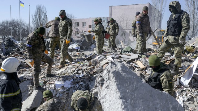 Tentara Ukraina dan petugas penyelamat mencari mayat di puing-puing di sekolah militer yang terkena roket Rusia, di Mykolaiv, Ukraina, Sabtu 19/3/2022). Foto: BULENT KILIC/AFP