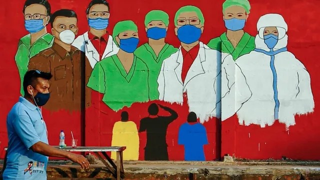 Warga yang menggunakan masker melintasi mural yang berisi pesan waspada penyebaran virus Corona di kawasan Tebet, Jakarta. Foto: Ajeng Dinar Ulfiana/REUTERS