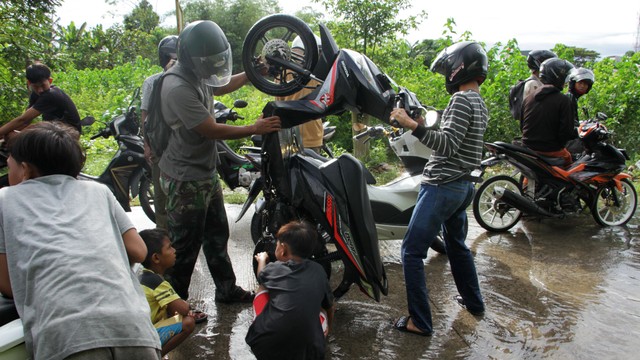 Pengendara berusaha mengeluarkan air dari knalpot motornya yang mogok usai menerobos banjir di Kecamatan Somba Opu, Kabupaten Gowa, Sulawesi Selatan, Jumat (27/5/2022). Foto: Arnas Padda/ANTARA FOTO