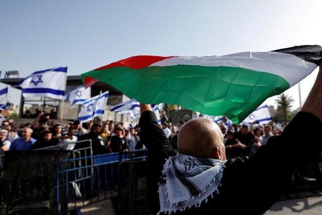 Seorang pria Palestina mengangkat bendera Palestina di seberang orang Israel yang memegang bendera Israel di Gerbang Damaskus ke Kota Tua Yerusalem. Foto: Ammar Awad/REUTERS