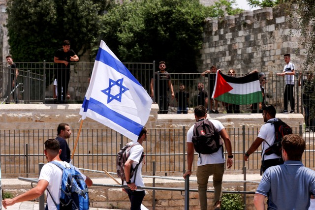 Warga Israel berdiri dengan bendera Israel berseberangan dengan warga Palestina dengan bendera Palestina di sebelah gerbang Damaskus ke Kota Tua Yerusalem. Foto: Ammar Awad/REUTERS