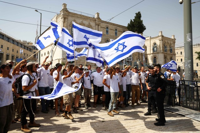 Pemuda Israel mengibarkan bendera dan bernyanyi ketika polisi berjaga sebelum mereka mulai berbaris di alun-alun di luar Kota Tua Yerusalem, Minggu (29/5/2022). Foto: Ronen Zvulun/REUTERS