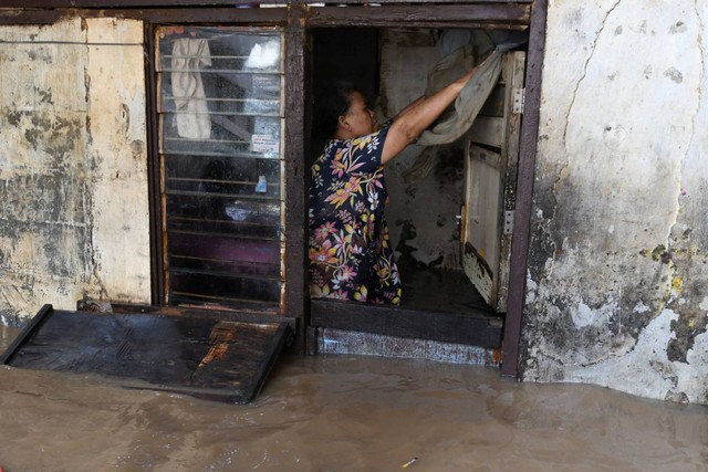 Seorang ibu membuka pintu rumahnya yang dilanda banjir di Kebon Pala, Kampung Melayu, Jakarta, Selasa (7/6/2022). Foto: Aditya Pradana Putra/ANTARA FOTO