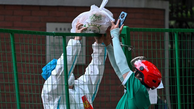 Pengantar makanan menyerahkan pesanan di jalan yang diblokir di daerah perumahan saat lockdown akibat kasus COVID-19 di distrik Huangpu, Shanghai, China pada Kamis (16/6/2022). Foto: Hector Retamal/AFP