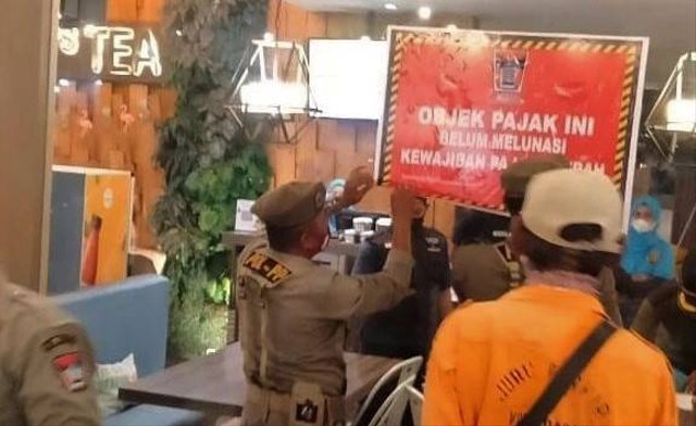 Personel Satpol PP Padang tengah memasang stiker menunggak pajak yang dipasang pada salah satu tempat usaha di Kota Padang, Sumatera Barat, Minggu 19 Juni 2022. Foto: dok Satpol PP