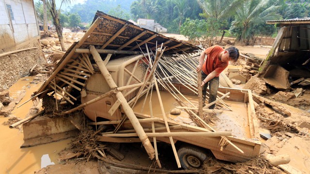 Warga membersihkan material yang menimpa mobil miliknya yang rusak akibat banjir bandang di Desa Purasari, Leuwiliang, Kabupaten Bogor, Jawa Barat, Kamis (23/6/2022). Foto: Yulius Satria Wijaya/Antara Foto