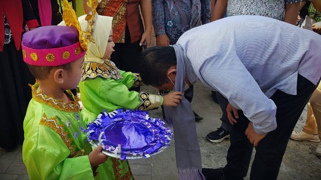 Penjabat Gubernur Gorontalo, Hamka Noer membungkuk saat menerima pengalungan kain karawo dari anak-anak PAUD Marhama. Selasa, (28/6). Foto: Dok banthayo