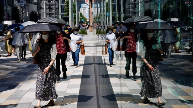 Pejalan kaki yang memegang payung tercermin di jendela saat gelombang panas melanda di Tokyo, Jepang, Selasa (28/6/2022). Foto: REUTERS/Issei Kato