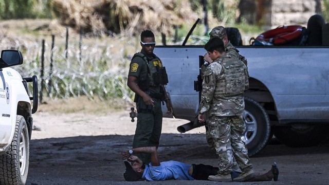 Seorang pria terbaring di tanah setelah diminta untuk duduk saat dia berdebat dengan petugas saat dia dan migran lainnya ditangkap oleh pasukan Patroli Perbatasan AS dan Garda Nasional di Eagle Pass, Texas, dekat perbatasan dengan Meksiko. Foto: Chandan Khanna / AFP