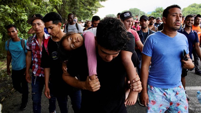 Seorang pria menggendong anaknya saat dia berjalan bersama dengan migran lain dalam karavan menuju perbatasan AS, di Tapachula, Meksiko, Jumat (1/7/2022). Foto: Jose Torres/REUTERS