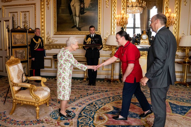 Ratu Elizabeth II dari Inggris mempersembahkan George Cross kepada Peter May, Sekretaris Tetap di Departemen Kesehatan dan Kepala Eksekutif Perawatan Kesehatan dan Sosial, dan Suster Joanna Hogg, Departemen Darurat Rumah Sakit Royal Victoria. Foto: Aaron Chown / POOL / AFP