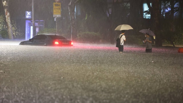 Pria menonton melihat yang ditinggalkan di daerah banjir saat hujan lebat di Seoul, Korea Selatan, Senin (8/8/2022). Foto: Yonhap via REUTERS