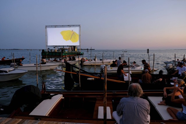 Orang-orang di atas kapal menghadiri pemutaran film di bioskop float-in selama acara 'Floating Cinema - Unknown Waters', yang berlangsung di perairan laguna Venesia, di Venesia, Italia. Foto: Manuel Silvestri/REUTERS