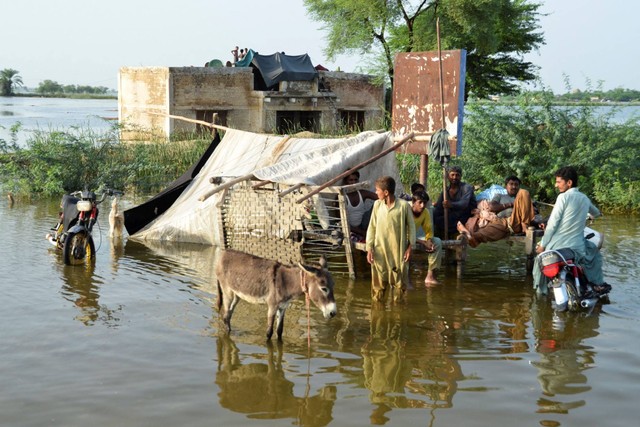 Orang-orang terlihat di luar rumah mereka yang terendam banjir, menyusul hujan dan banjir selama musim hujan di Suhbatpur, Pakistan, Minggu (28/8/2022). Foto: Amer Hussain/REUTERS