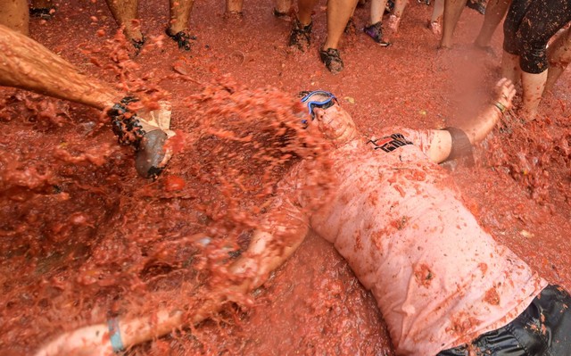 Seorang pria yang bersuka ria berbaring di atas bubur tomat saat mengikuti festival tahunan "Tomatina" di kota timur Bunol, Spanyol, Rabu (31/8/2022). Foto: Jose Jordan/AFP