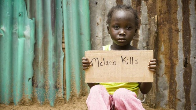 Seorang anak di Afrika memegang tanda bertuliskan "Malaria membunuh"