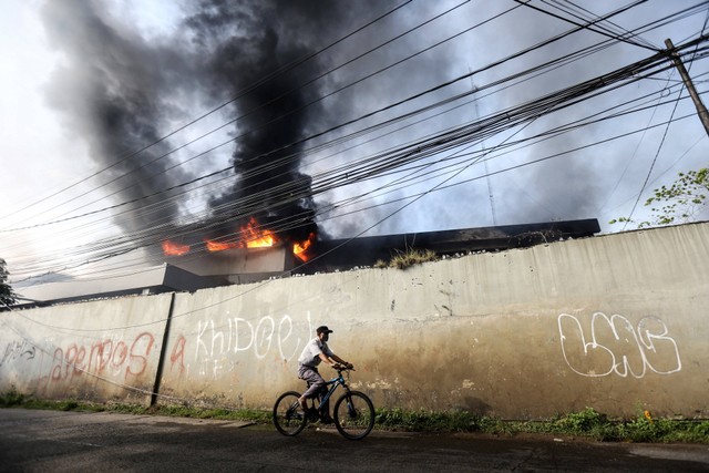 Warga melintas di samping gudang JNE yang terbakar di Pekapuran, Depok, Jawa Barat, Senin (12/9/2022). Foto: Asprilla Dwi Adha/Antara Foto