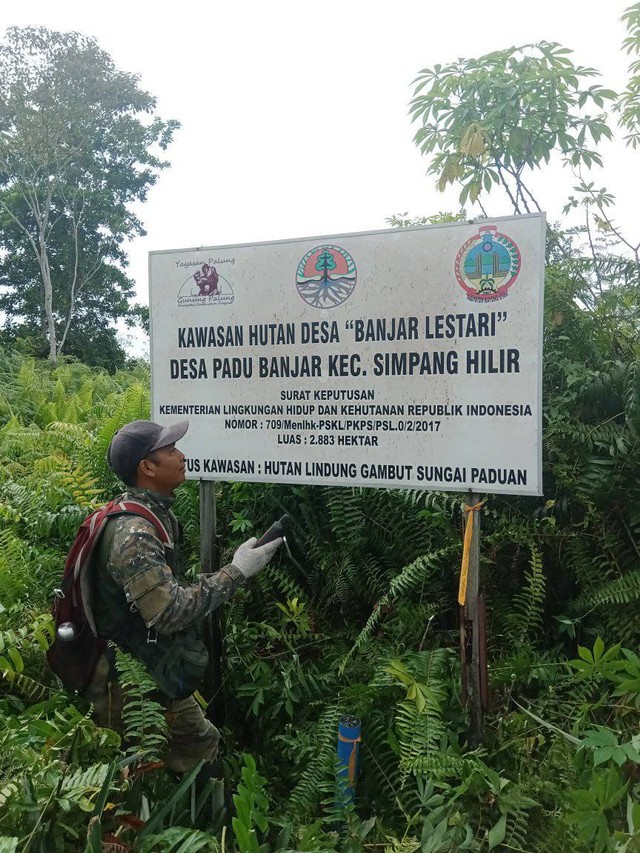 Samsidar saat berfoto di papan plang hutan desa Padu Banjar. (Foto : Samsidar).