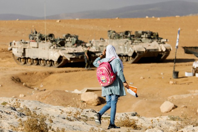 Seorang siswa Palestina berjalan melewati tank tentara Israel dalam perjalanan ke sekolah, di Masafer Yatta dekat Hebron di Tepi Barat. Foto: Mussa Qawasma/REUTERS
