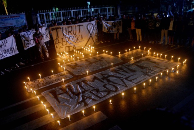 Sejumlah suporter PSM Makassar berdoa saat melakukan aksi menyalakan lilin di depan Monumen Mandala, Makassar, Sulawesi Selatan, Minggu (2/10/2022) malam. Foto: Abriawan Abhe/Antara Foto