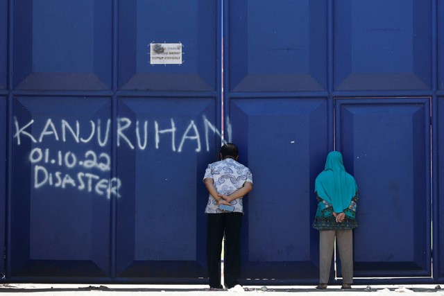 Orang-orang mengintip melalui gerbang Stadion Kanjuruhan di Malang, Jawa Timur, Selasa (4/10/2022). Foto: Willy Kurniawan/REUTERS