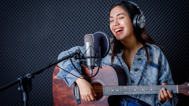 Seorang wanita mengenakan Headphone dengan bermain gitar di studio. Foto: Thinnapob Proongsak/Shutterstock.