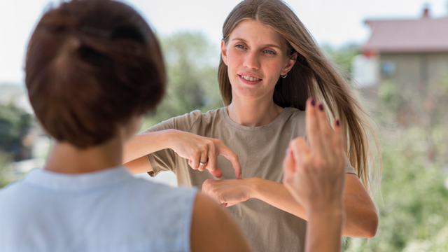 Woman using sign language while outdoors converse with her friend (freepik.com)