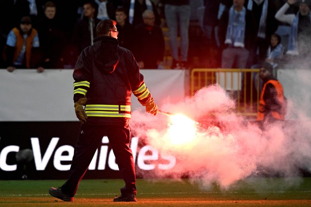 Seorang petugas polisi memegang kembang api yang dilempar oleh seorang penggemar ke lapangan di Stadion Eleda, Malmo, Swedia. Foto: Johan Nilsson/TT News Agency/Reuters