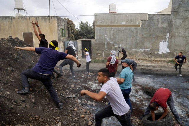 Para pengunjuk rasa Palestina melemparkan batu di tengah bentrokan dengan tentara Israel saat demonstrasi menentang pengambilalihan tanah Palestina oleh Israel di desa Kfar Qaddum di Tepi Barat, pada Jumat (7/10/2022). Foto: Jaafar Ashtiyeh/AFP