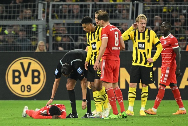 Pemain Bayern Muenchen Alphonso Davies (kiri) cedera saat hadapi Dortmund di Signal Iduna Park, Dortmund, Jerman, Sabtu (8/10/2022). Foto: Ina Fassbender/AFP