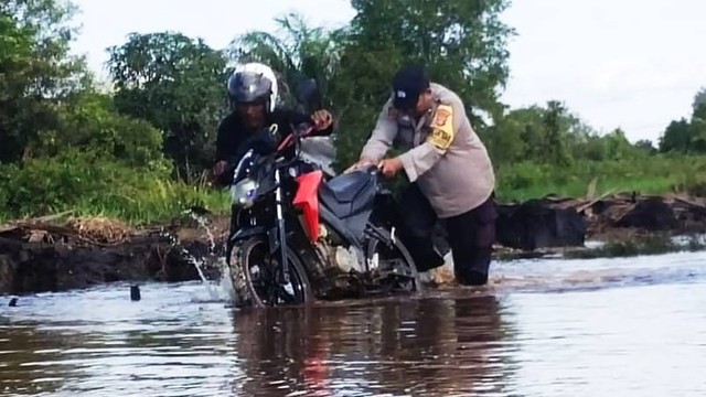 Bhabinkamtibmas Kelurahan Raja Seberang dan Mendawai Seberang, Aipda Akhmad Japar sata membantu warga yang mogok saat situasi Jalan Pangkalan Bun-Kotawaringin Lama terendam banjir. Foto: Lukman Hakim/InfoPBUN