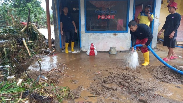 Warga dan relawan membersihkan sebuah warung yang dipenuhi lumpur akibat banjir. Foto/Aisyah Nawangsari